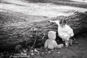 retrato de niña con su osito junto al tronco de un árbol caído