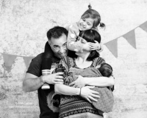 foto de familia con una niña subida a caballito sobre su padre que abraza la cabeza de su mamá