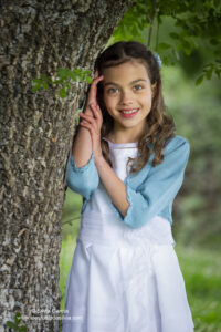 retrato de niña vestida de primera comunión apoyada en un árbol
