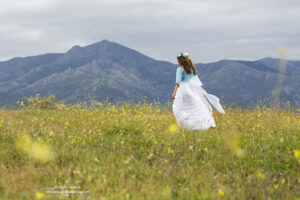 niña vestida de primera comunión de espaldas caminando entre las flores y la Maliciosa de fondo