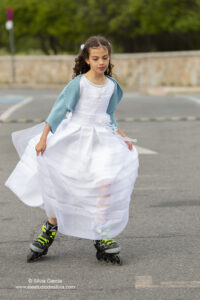 niña vestida de primera comunión patinando en la calle